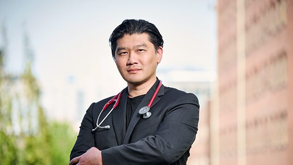 David Lin, a man wearing a stethoscope stands confidently in front of the Bloodworks Bio building.