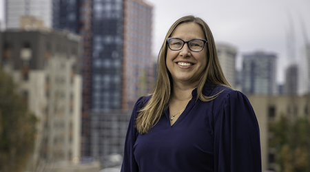 Andrea Bradford, a woman in a blue shirt standing in front of a city.