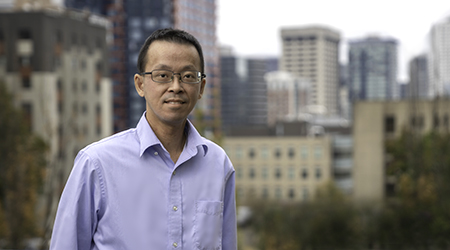 Lin Tsai, a man in a blue shirt standing in front of a city.